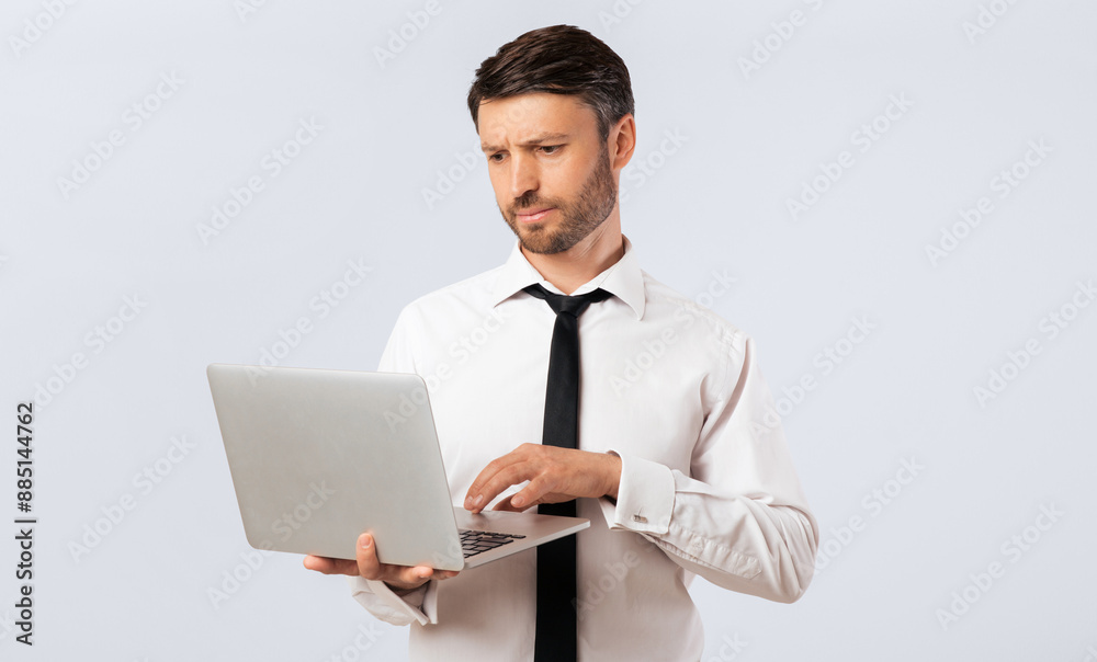A businessman in a white shirt and black tie is working on his laptop. He looks concerned as he types on the keyboard.