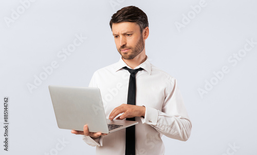 A businessman in a white shirt and black tie is working on his laptop. He looks concerned as he types on the keyboard.