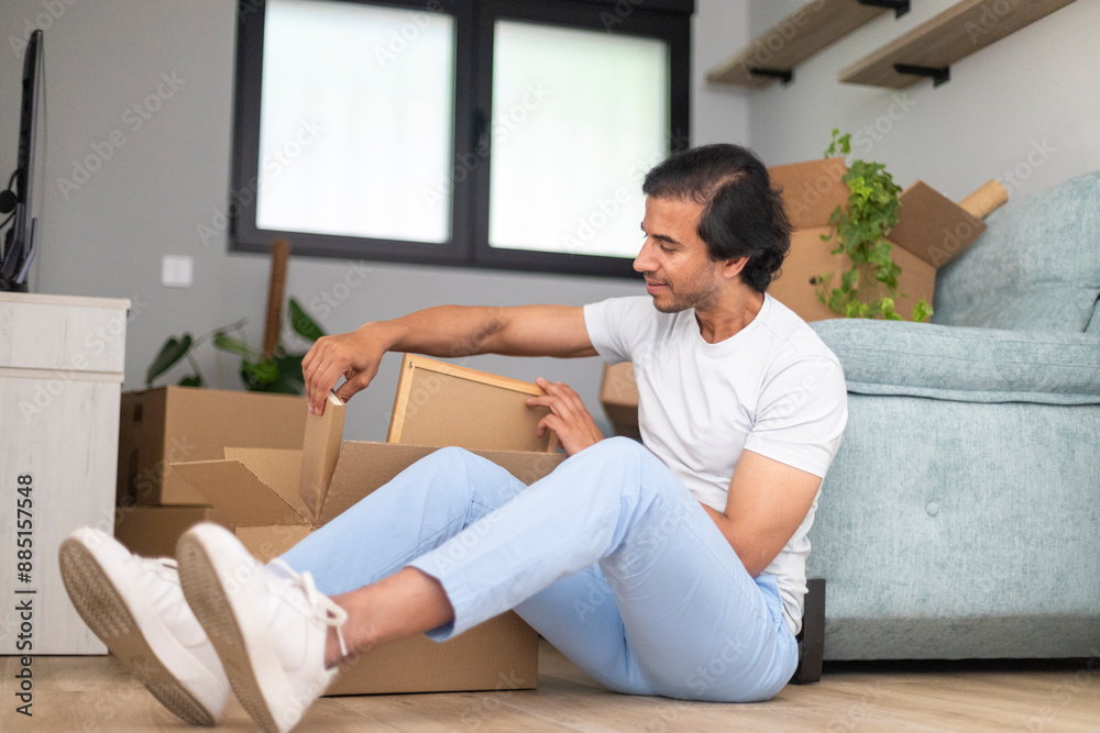 Man comfortably unpacking a box while sitting on the floor in his new home. Man comfortably unpacking a box while sitting on the floor in his new home.