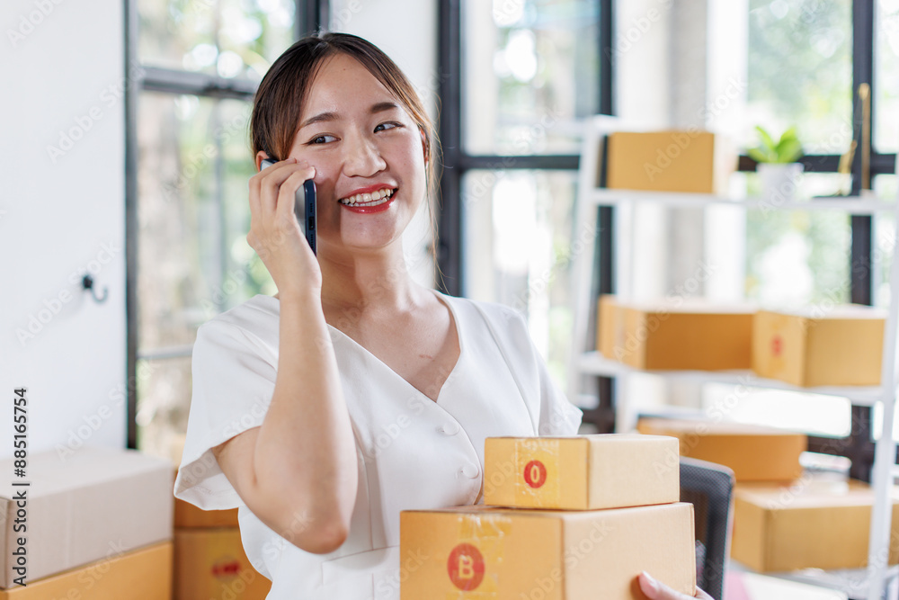 Young asia seller woman happy work on laptop busy cellphone call chat to customer at home office desk use digital tablet computer in SME online store social e-commerce sale page service web support.
