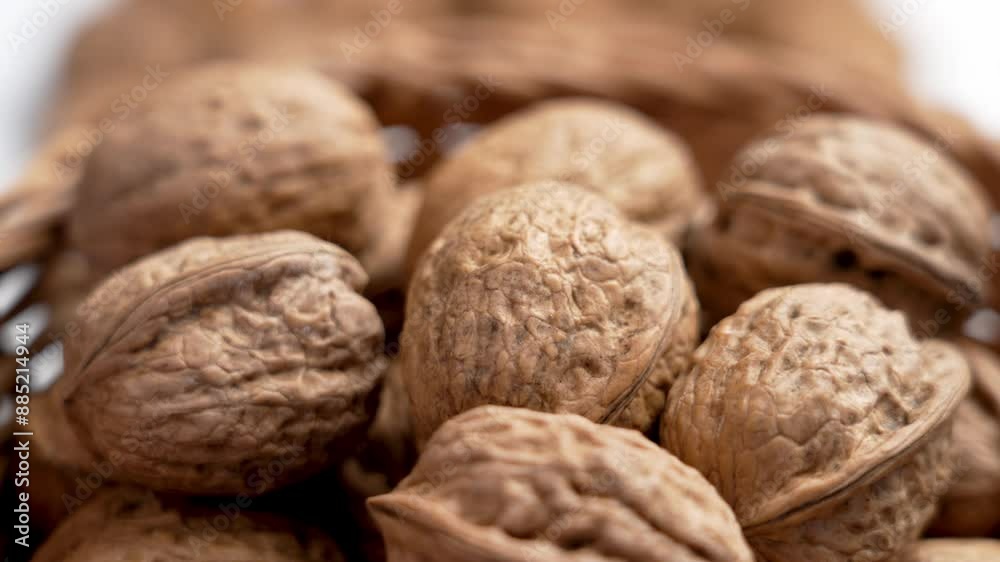 Whole walnuts in wooden rattan bowl, their shells showing intricate patterns and textures. They are ready to be cracked open, revealing the delicious nut inside. Rotation. Close up Whole walnuts in wooden rattan bowl, their shells showing intricate patterns and textures. They are ready to be cracked open, revealing the delicious nut inside. Rotation. Close up