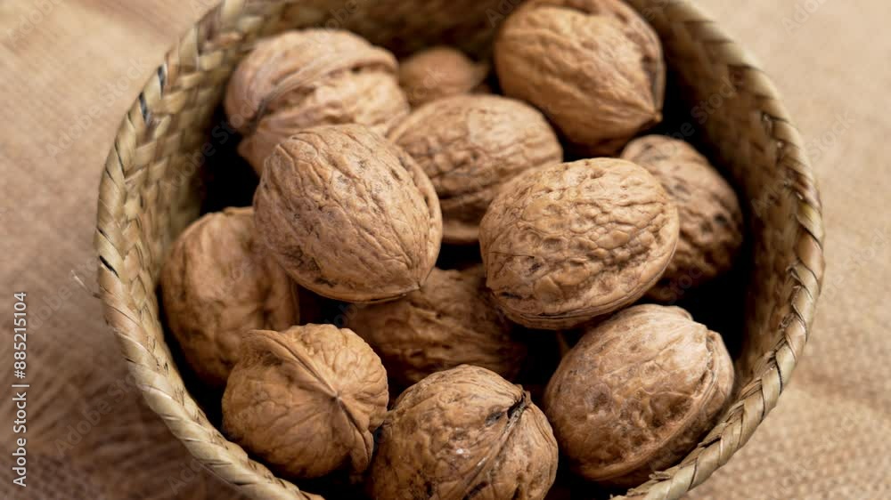 Organic unshelled walnuts as a source of protein and fiber in a rustic wicker bowl on rough burlap. Whole nutritious nuts. Rotation. Top view Organic unshelled walnuts as a source of protein and fiber in a rustic wicker bowl on rough burlap. Whole nutritious nuts. Rotation. Top view