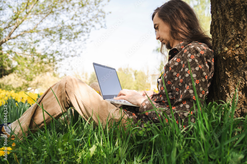 Man using laptop leaning on tree trunk at meadow Man using laptop leaning on tree trunk at meadow