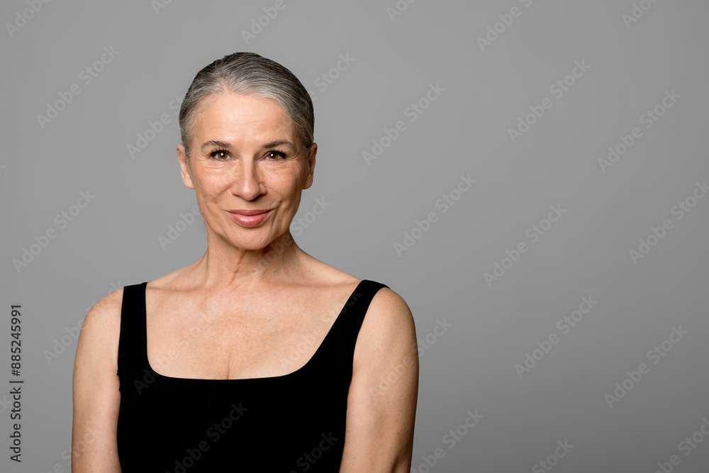 Smiling senior woman in black sportswear against gray background