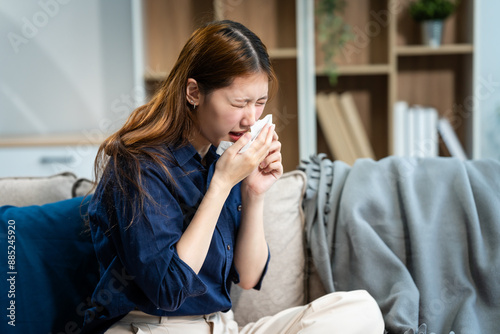 Obraz na płótnie A young Asian woman sits on a sofa, feeling sick with a cold