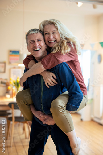 Happy senior man piggybacking blond woman at home
