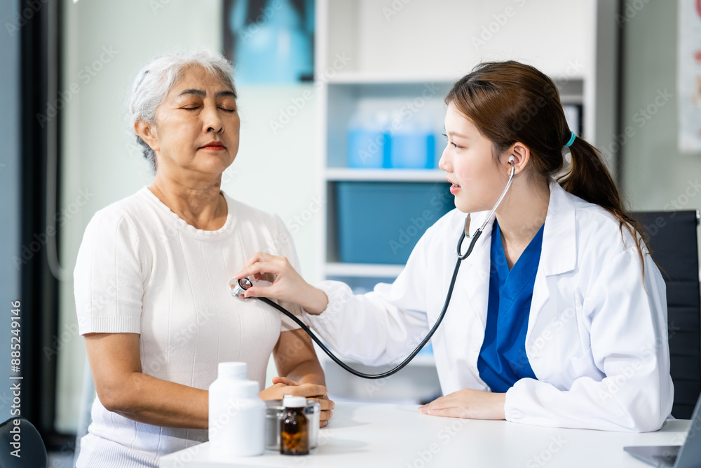 A young female nurse works at a desk with a grey-haired Asian mature woman, discussing heart-related conditions like heart disease, heart attack, and hypertension. A young female nurse works at a desk with a grey-haired Asian mature woman, discussing heart-related conditions like heart disease, heart attack, and hypertension.