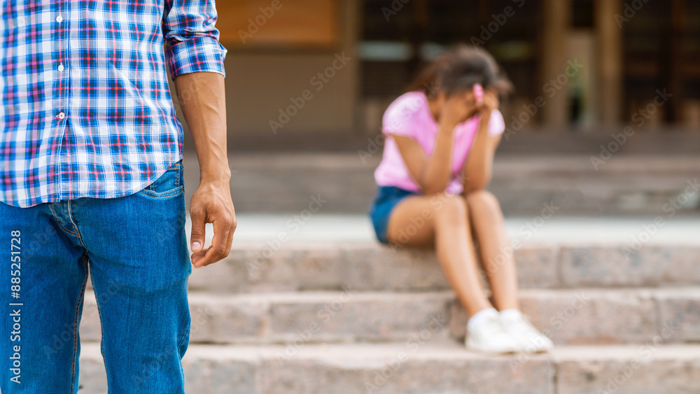 Guy stands near a girl sitting on steps. The girl is sitting with her head in her hands and appears to be sad. Guy is looking away from the girl Guy stands near a girl sitting on steps. The girl is sitting with her head in her hands and appears to be sad. Guy is looking away from the girl