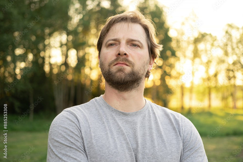 Portrait of handsome young man in gray t-shirt outdoors. Male with long hair and beard feel happy, calm and serious on Green nature sunset background. Man looking away into distance. Diversity People Portrait of handsome young man in gray t-shirt outdoors. Male with long hair and beard feel happy, calm and serious on Green nature sunset background. Man looking away into distance. Diversity People