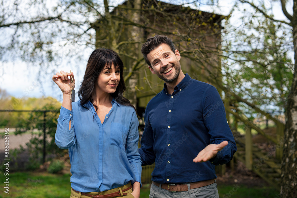 Smiling businessman standing with businesswoman holding house keys in back yard Smiling businessman standing with businesswoman holding house keys in back yard