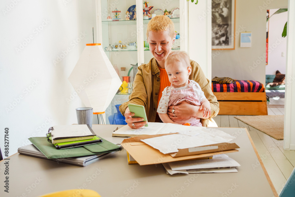 Smiling mother sitting with toddler daughter and using smart phone at home Smiling mother sitting with toddler daughter and using smart phone at home