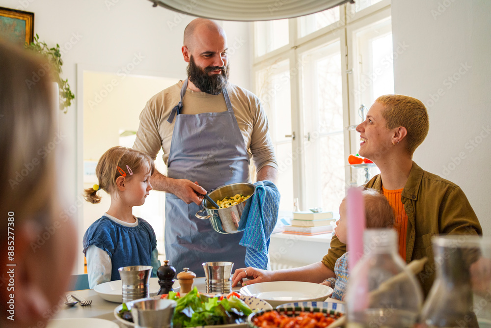 Man serving food to family sitting at dining table in home Man serving food to family sitting at dining table in home