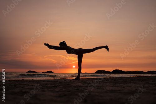 Silhouette of sport woman performing a yoga pose on the beach at sunset, with the sun setting behind the horizon and the calm sea .Yoga is meditation and healthy sport relaxing on summer holiday