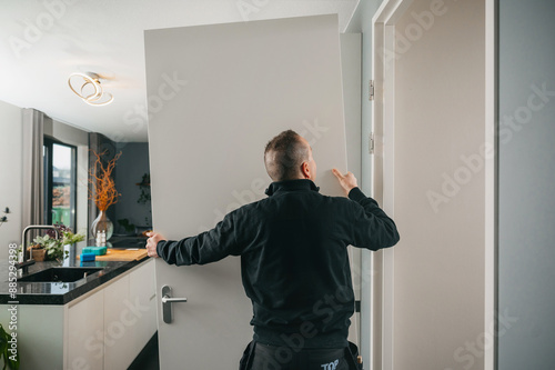 Carpenter installing white wooden door into doorframe