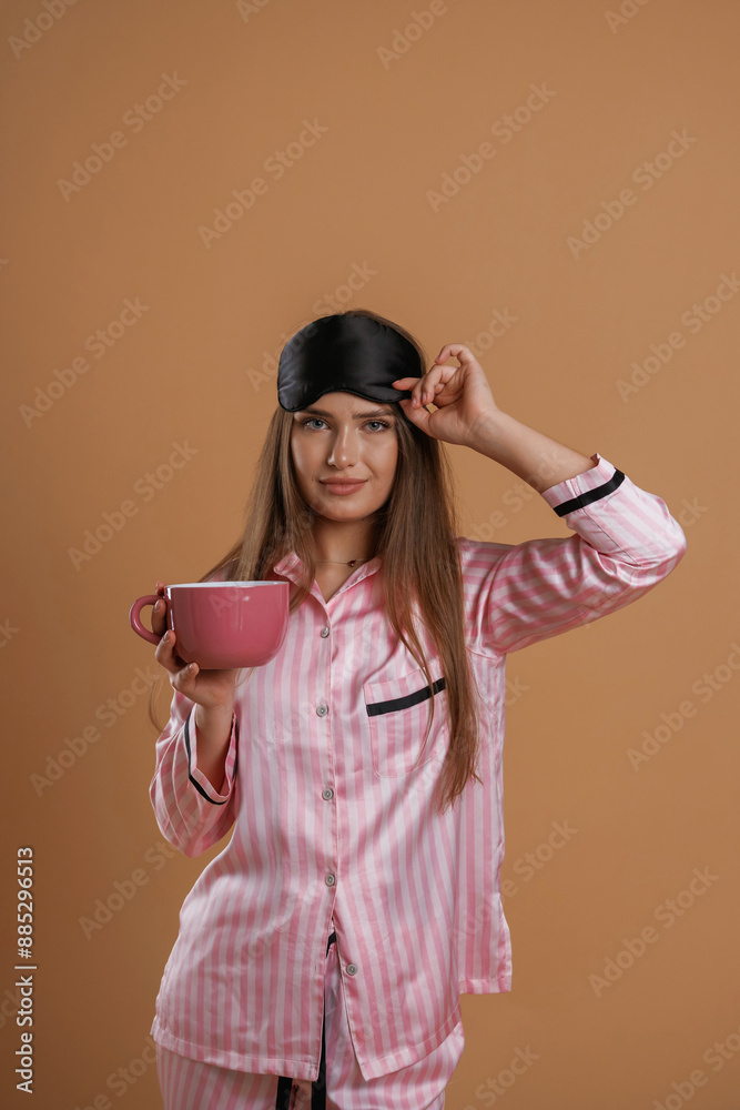 Pink pajama, with cup of drink. Young pretty woman is against background in the studio Pink pajama, with cup of drink. Young pretty woman is against background in the studio