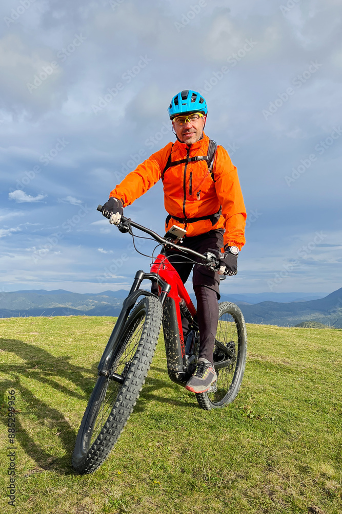 Cyclist man riding electric mountain bike outdoors. Male tourist biking along grassy trail in the mountains, wearing helmet and backpack. Concept of sport, active leisure and nature. Cyclist man riding electric mountain bike outdoors. Male tourist biking along grassy trail in the mountains, wearing helmet and backpack. Concept of sport, active leisure and nature.