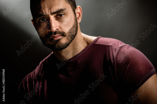 Portrait of strong handsome man with brutal unshaven face posing on dark background, Dark allure: Young man's serious gaze and beard create a powerful portrait against a gray background.