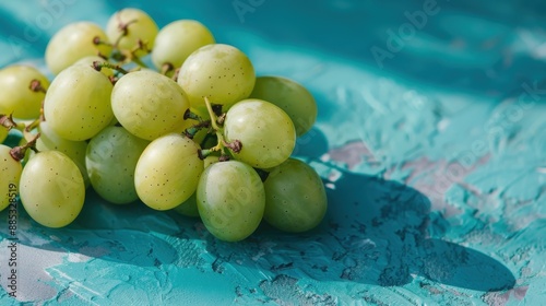 A cluster of plump green grapes rests on a richly hued turquoise surface, creating a visually striking contrast that enhances the fruit's natural appeal. photo