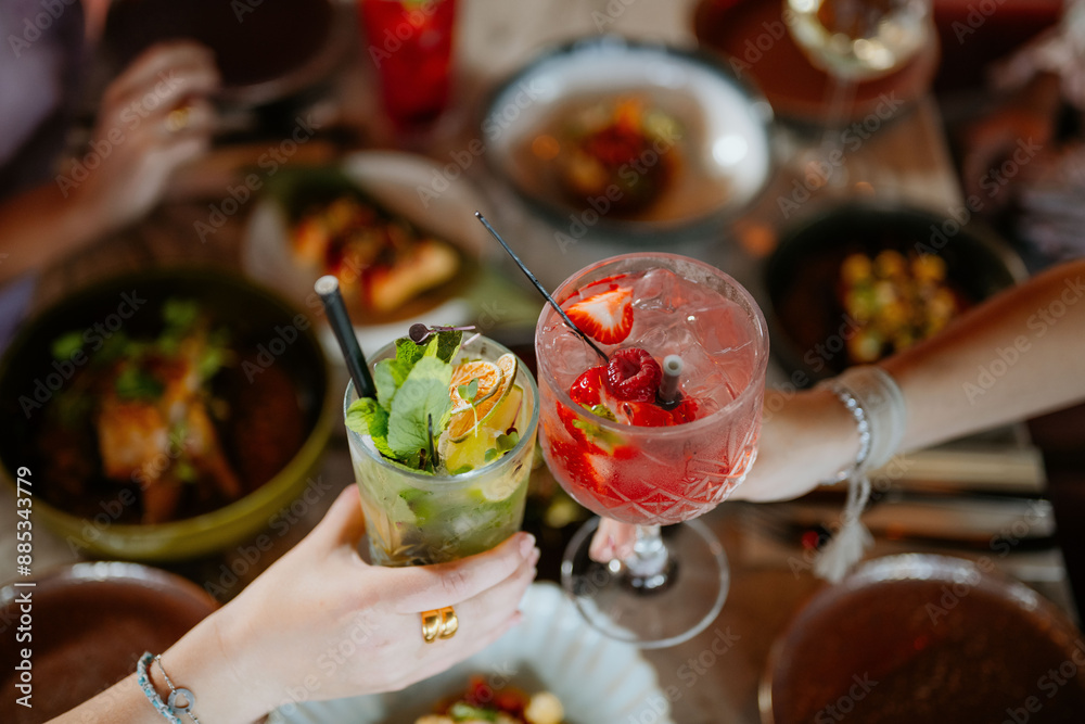 Close-up shot of two cocktails above a filled restaurant table full of food Close-up shot of two cocktails above a filled restaurant table full of food