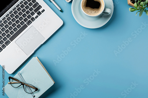 Top view of office desk with laptop, coffee cup and notebook on blue background for work online concept. Flat lay, top view, copy space, stock photo. In the style of stock photo.