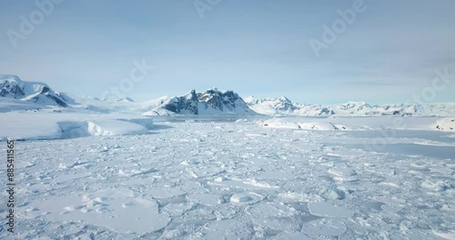 Beautiful winter panorama arctic nature landscape. Aerial fly over frozen polar ocean and snow covered mountains under blue sky. People explore Antarctica discover South Pole beauty. Expedition travel