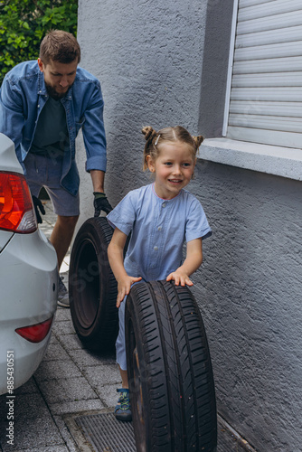Cuadro en lienzo Cute little girl helps her father to change wheel on their family car on warm da