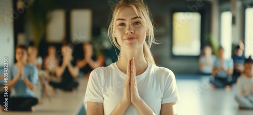 A beautiful blonde woman with folded hands doing a yoga pose standing at the front on a blurred background.