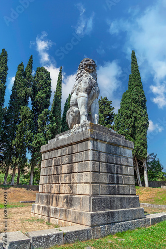 The Lion of Chaeronea, an ancient marble monument in Boeotia, Greece, standing majestically against a blue sky and surrounded by lush cypress trees. It's a nearly 6 m (20 ft) tall funerary monument.  photo