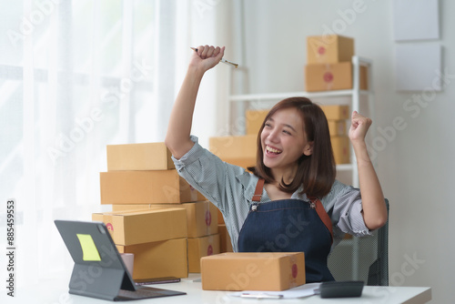 Excited woman celebrating successful online business with cardboard packages and laptop in home office workspace.