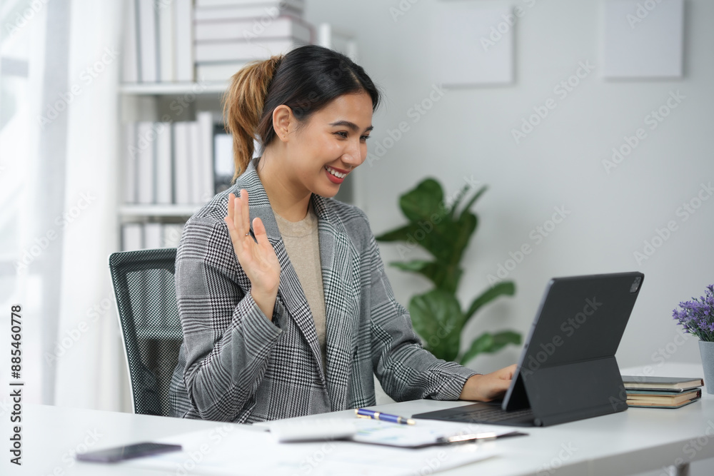 Professional woman conducting video conference at home office, working remotely, waving and smiling at laptop during virtual meeting. Professional woman conducting video conference at home office, working remotely, waving and smiling at laptop during virtual meeting.