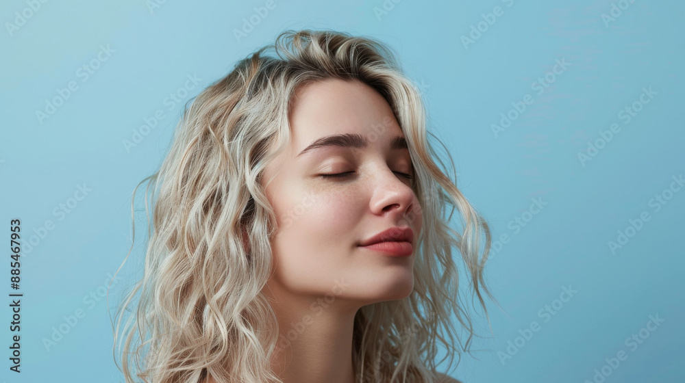 A serene close-up of a young woman with closed eyes, basking in soft, gentle light against a simple blue background. A serene close-up of a young woman with closed eyes, basking in soft, gentle light against a simple blue background.