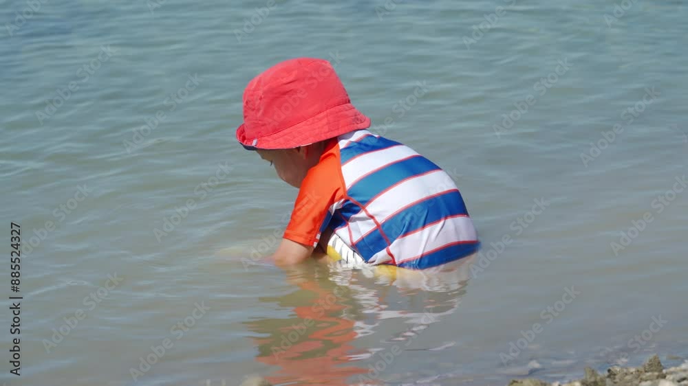 Small child wearing sun protection shirt playing on the lake shore on a summer day. Small child wearing sun protection shirt playing on the lake shore on a summer day.