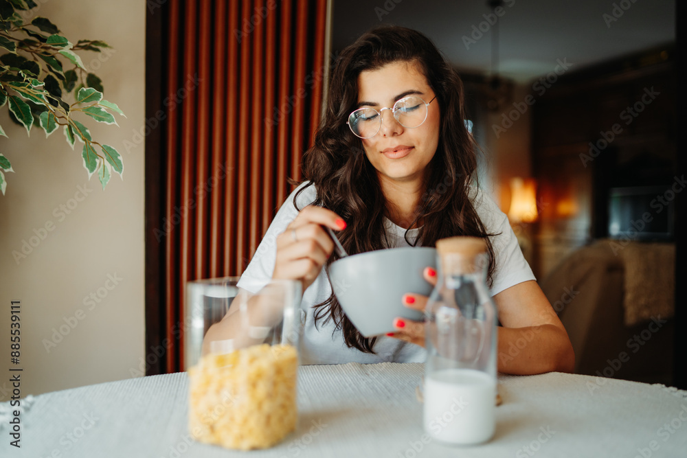 One young beautiful caucasian woman wearing glasses and eating corn flakes or cereal for breakfast One young beautiful caucasian woman wearing glasses and eating corn flakes or cereal for breakfast