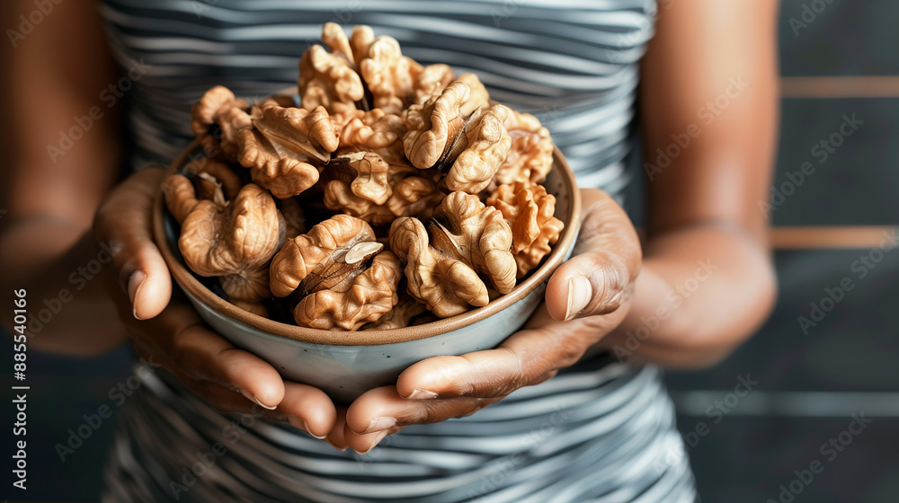 The image shows hands holding a bowl of fresh shelled walnuts. The rich tones, dark grey background and the careful presentation emphasize healthy nutrition and a balanced diet The image shows hands holding a bowl of fresh shelled walnuts. The rich tones, dark grey background and the careful presentation emphasize healthy nutrition and a balanced diet