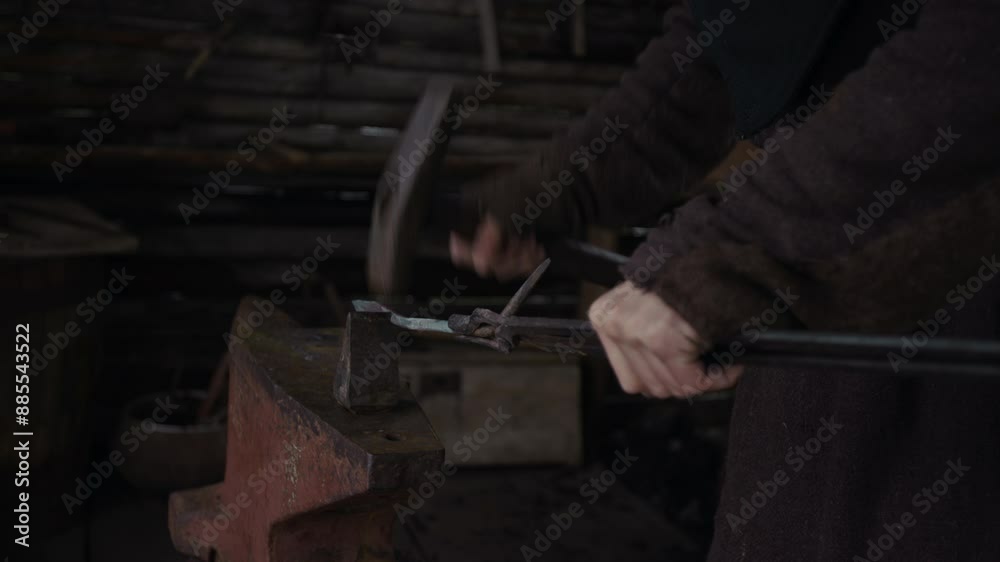 Close-up shot of hands of anonymous craftsman holding iron nail or fixture with tongs and forging it with hammer on anvil, while working in smithy Close-up shot of hands of anonymous craftsman holding iron nail or fixture with tongs and forging it with hammer on anvil, while working in smithy