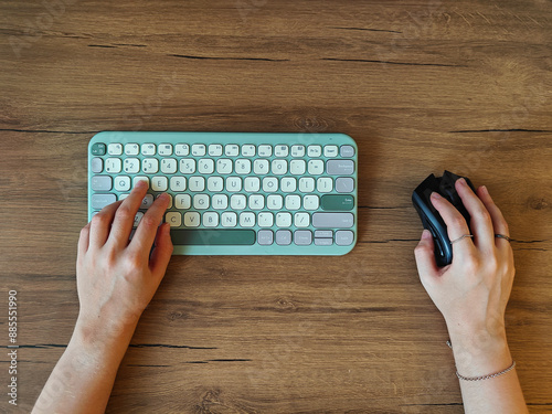 Top view of woman using a keyboard and computer mouse on a brown wooden table