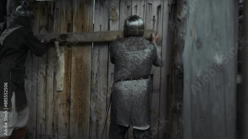 Medium full slowmo shot of two medieval guards in chainmail, steel helmets hastily barring wooden gate of fortress or garrison, then running off photo