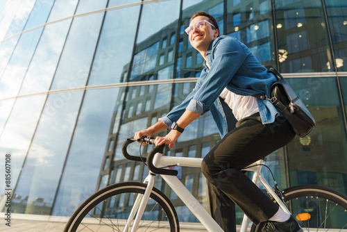 A cheerful young man cycling past a modern glass building, exuding energy and happiness in an urban setting.