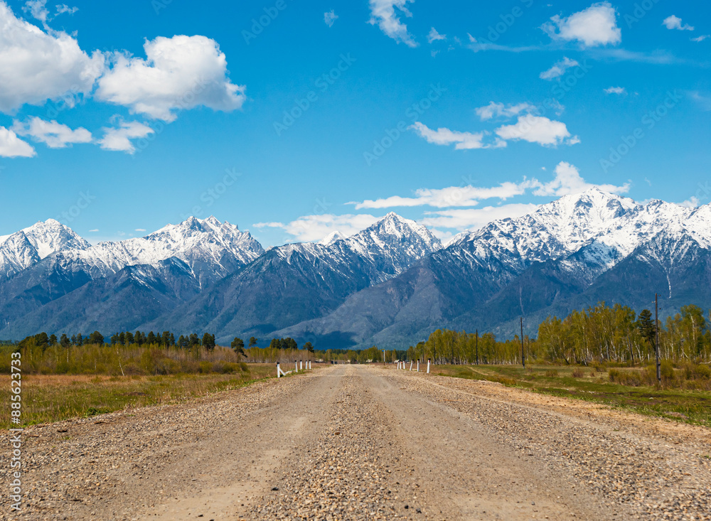 Fototapeta premium A winding gravel road leading toward snow-capped mountains