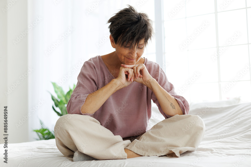 Mature woman in linen clothes relaxing on bed at home Mature woman in linen clothes relaxing on bed at home
