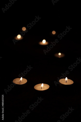 Round small candles in the dark. Lighting a candle, praying, hoping for the best. Religious atmosphere, candle fire on a black background © Yaroslav