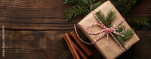 Christmas present on a wooden background. The gift is wrapped in brown paper with red twine, cinnamon and pine branches. Winter holiday decor. Horizontal banner with copy space to text.