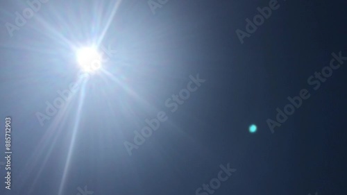 Brilliant Sun in Clear Blue Sky with Lens Flare and Orb Reflection - Natural Light Phenomenon in Midday Summer Sky - Radiant Sunshine Beams and Atmospheric Effects