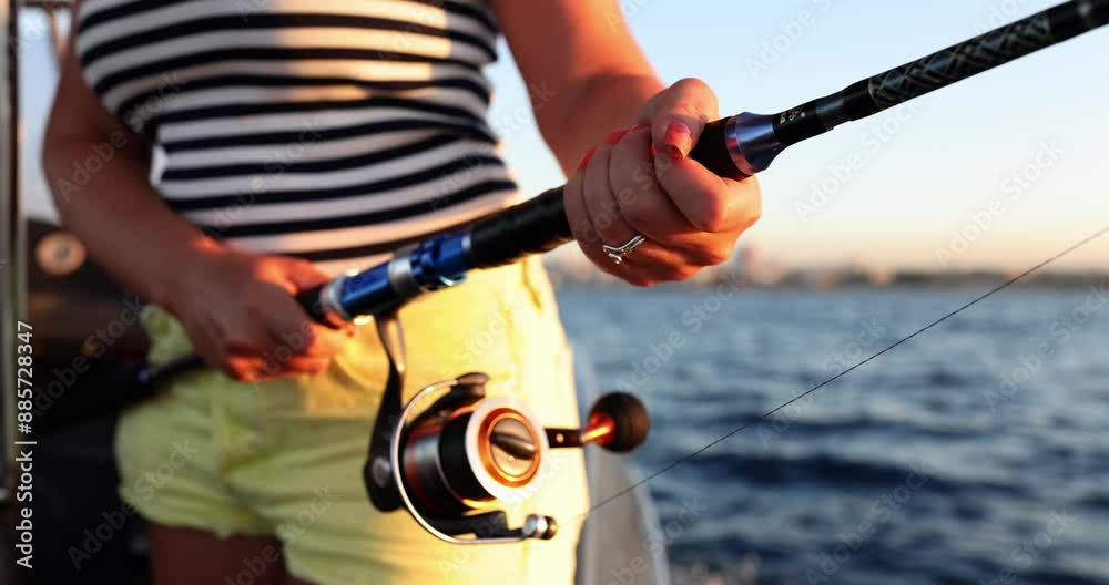 Woman with rod fishes standing on sailing motorboat at summer sunset slow motion. Lady catches fish during sea journey. Active hobby and lifestyle