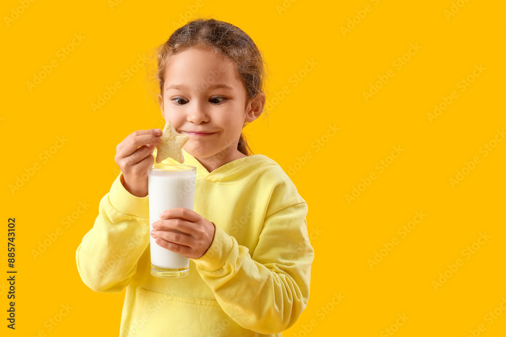 Cute little girl with tasty cookie and glass of milk on yellow background Cute little girl with tasty cookie and glass of milk on yellow background
