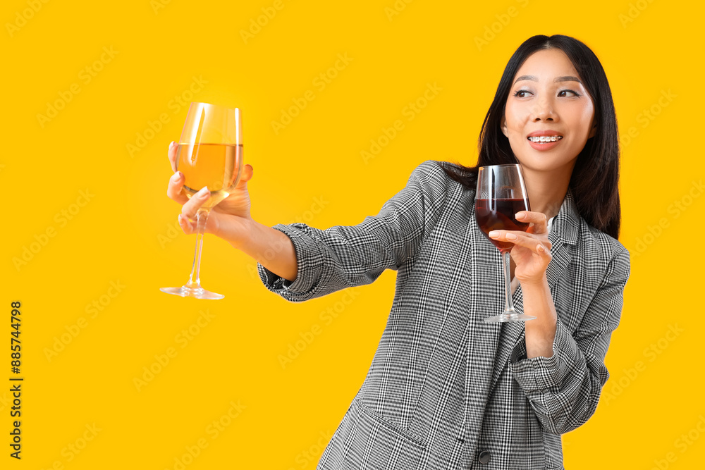 Beautiful Asian businesswoman with glasses of wine on yellow background