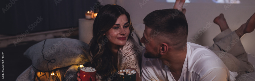 Fototapeta premium Banner. Romantic surprise for girlfriend or boyfriend for Saint Valentine's Day. Bedroom prepared for watching movies decorated with lights, candles. Cozy home Christmas atmosphere, hot chocolate