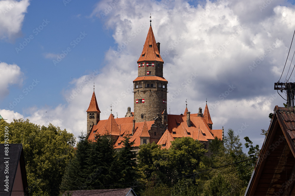 Fototapeta premium an old stone castle with a red roof and round towers. A castle on a wooded hill. Nature, landscape, castle. Medieval. Blue sky with clouds above the castle.