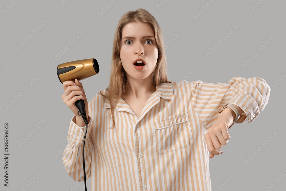Shocked young woman with hair dryer checking time on wristwatch against grey background Shocked young woman with hair dryer checking time on wristwatch against grey background
