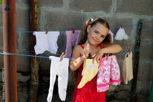 little girl washes children's clothes and hangs them to dry on a line